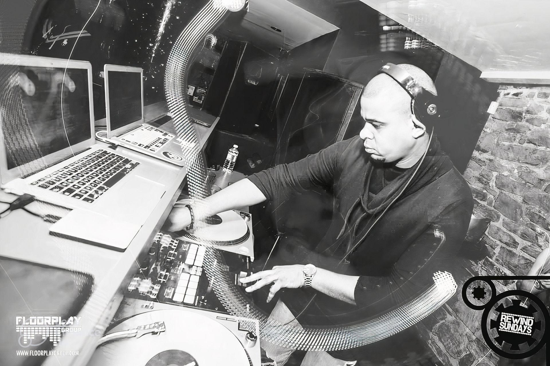 DJ performing in a club with turntables and laptops, surrounded by audio equipment and brick walls.